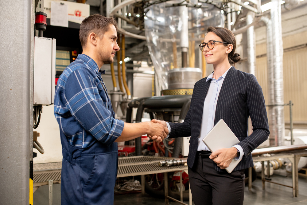 Happy young female partner shaking hand of engineer of chemical processing factory after making deal